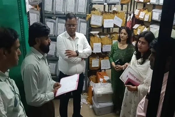 रिकॉर्ड रूम में फाइलों और अभिलेखों से भरी रैक के बीच अधिकारियों तथा महिलाओं से बातचीत करते कलेक्टर शिवम वर्मा